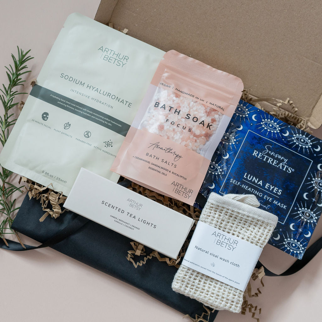 Letterbox gift with bath salts, self heating eye mask, 3 scented soy wax tealights, natural sisal face cloth and moisturising facemask on cream background. All letterbox gifts are sent with a handwritten note and include postage.