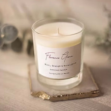 Large clear glass soy wax candle from Florence green. Scent of mint orange and eucalyptus on a beige background.