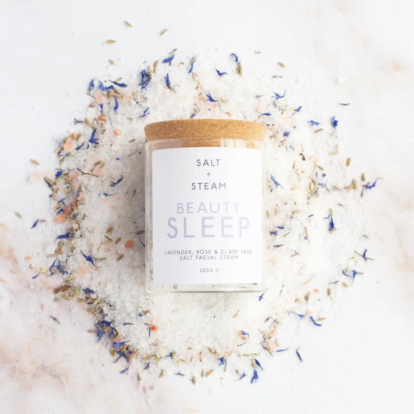 Glass jar of lavender and rose vegan bath salts from British brand Salt and steam on a white background with added flower petals for decoration