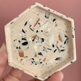 Pale terracotta coloured handmade hexagon trivet dish from eco resin useful for jewellery on a pink background